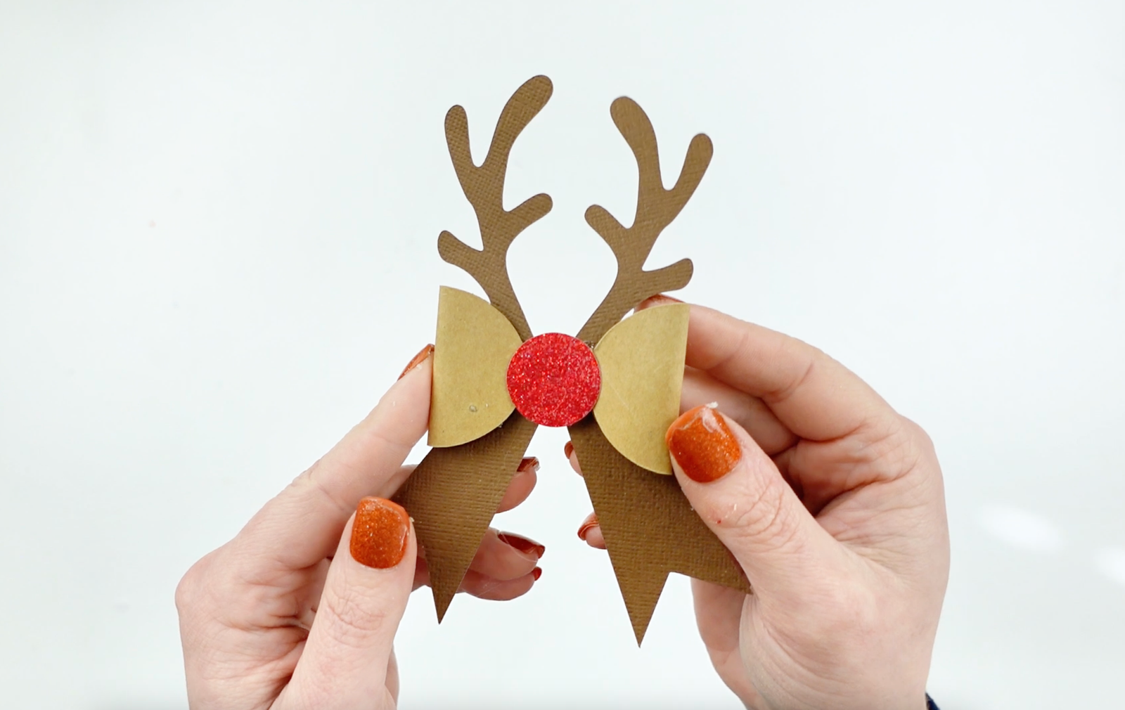 A DIY Christmas Reindeer Bow made out of paper in brown and tan with reindeer antlers and a red "nose". Free SVG Template download to create your own holiday bows.